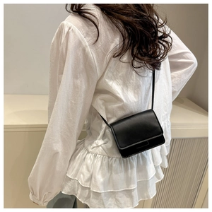 Detailed view of a small black rectangular crossbody bag styled on a white ruffled shirt