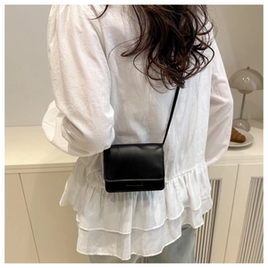 Rear view of a model wearing a minimalist black mini crossbody bag with a slim shoulder strap