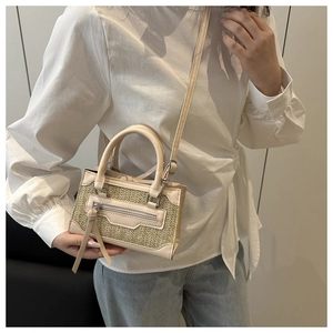 Dettaglio di una piccola borsa a tracolla in paglia con finiture in pelle color crema e nappina