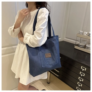 Close-up of a blue denim tote bag with a leather fashion tag on a white dress