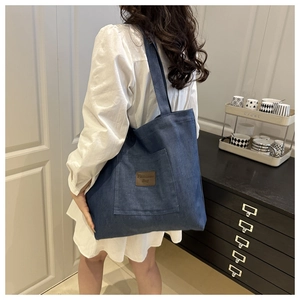 Detail view of large denim tote bag featuring an outer pocket and brown leather patch decoration