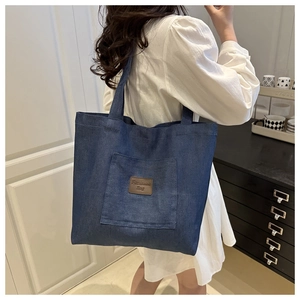 Detail of blue denim tote bag with brown leather patch and large front pocket for storage