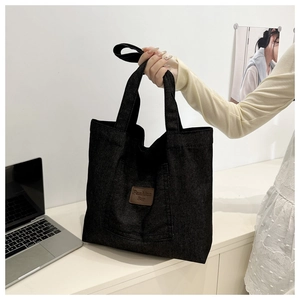 Detail of the brown leather brand tag on a large black denim tote bag for commuting
