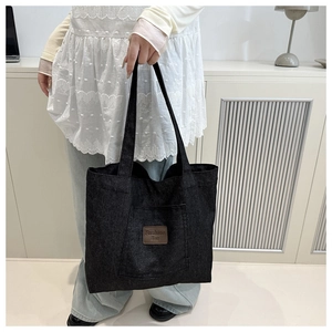 Detail of black denim tote bag with brown leather 'Fashion Bag' logo and stitching
