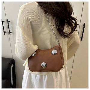 Brown leather underarm bag with large silver studs and metallic chain strap shown on model