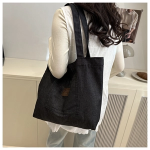 Détail d'un sac cabas noir montrant la poche latérale et l'étiquette en cuir décorative
