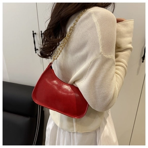 Detail of red glossy leather crescent shoulder bag with golden chain strap on model