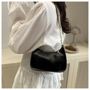 Close-up of black half-moon shoulder bag with elegant gold chain strap on a model