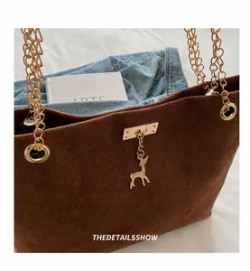 Dettaglio borsa tote in pelle scamosciata marrone con catena dorata e ciondolo a cervo
