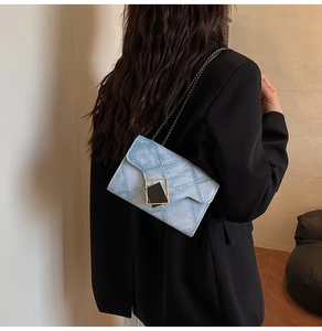 Detail view of light blue quilted chain crossbody bag with geometric metal buckle on a model