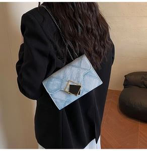 Détail du sac à bandoulière en denim matelassé bleu avec chaîne noire porté par un mannequin