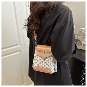 Detail of a chic crossbody bag with M-pattern and golden heart clasp shown on a model