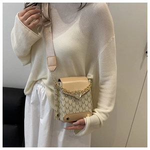 Detail of beige crossbody bag with M-pattern print, heart clasp, and wide strap