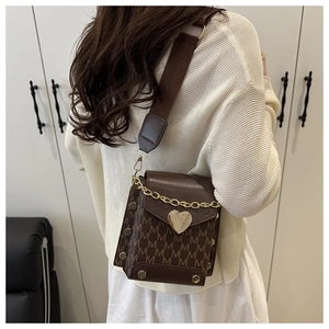 Detail of a brown crossbody bag with letter print and heart-shaped metal buckle worn by model