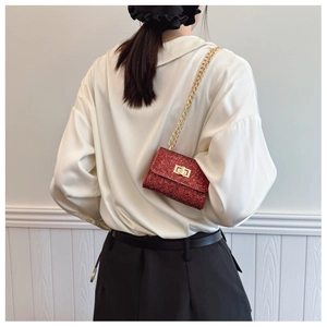 Gros plan du mini sac à paillettes rouges avec chaîne dorée et fermoir porté par le modèle
