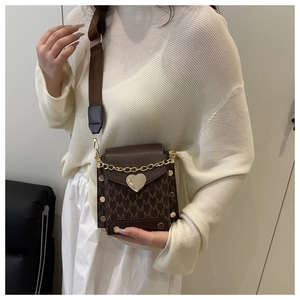 Detalle de bolso bandolera marrón con estampado M y cierre de corazón dorado