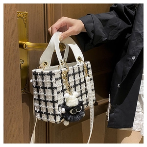 Dettaglio borsa a mano in tweed bianco e nero con finiture dorate e ciondolo di peluche
