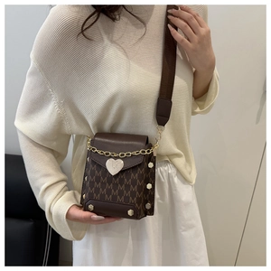 Detail view of small brown crossbody bag with M-pattern print and heart-shaped metal buckle