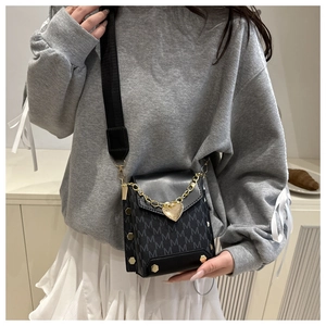 Detail of black crossbody bag with gold heart chain and monogram pattern on model