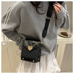 Detail of crossbody bag featuring M-pattern, gold heart charm, and metallic rivet studs