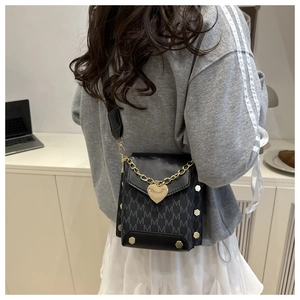 Detail of black crossbody bag with M-pattern jacquard and gold heart charm decoration