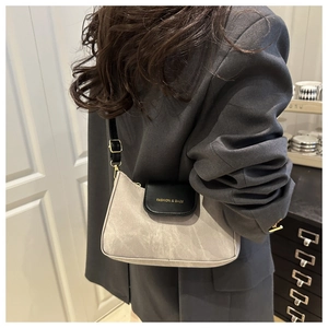 Detail of grey suede shoulder bag with black leather flap and gold FASHION & BAGS text