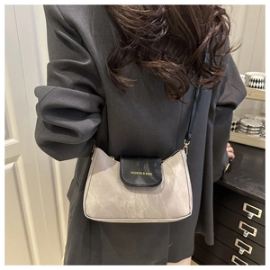 Detail of a grey textured crossbody bag with a black leather flap and fashion lettering