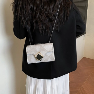 Fashionable grey quilted crossbody bag with metal buckle and chain strap on a model