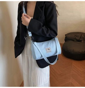 Detail of light blue denim cylinder bag with a cartoon patch and adjustable shoulder strap
