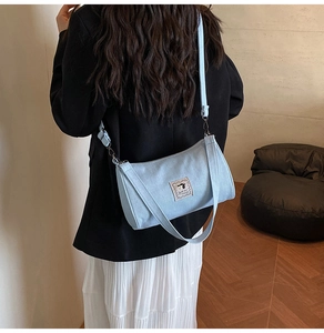 Detail of light blue denim barrel bag with embroidered patch worn by a model
