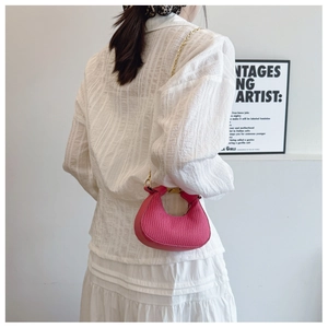 Détail du mini sac croissant rose vif avec texture plissée et bandoulière chaîne dorée