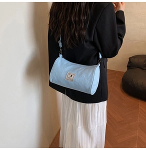 Detailed back view of a light blue cylindrical crossbody bag on model for casual styling