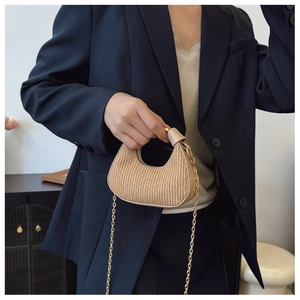 Détail du sac croissant plissé beige avec chaîne dorée sur fond de blazer bleu marine