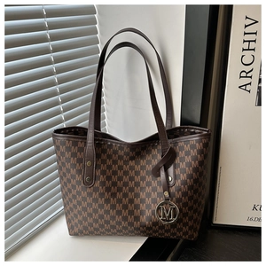 Detail of dark brown tote bag featuring all-over M-letter print and metallic M-charm