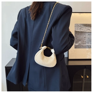 Détail du sac demi-lune beige plissé avec chaîne dorée sur un blazer marine