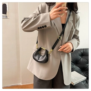 Close-up of mini black leather crossbody bag with gold buckle on a grey blazer outfit