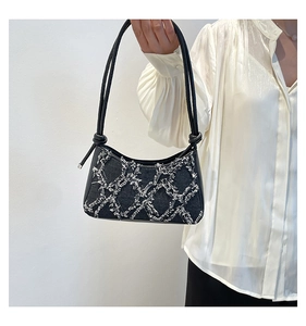 Detail of black quilted denim underarm bag with white stitching and knotted shoulder strap