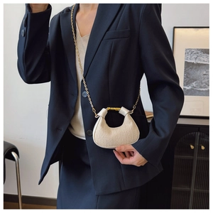 Détail du sac croissant plissé crème avec chaîne dorée sur un blazer bleu marine