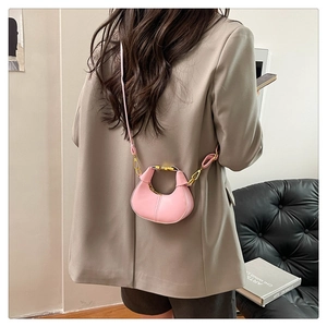 Mini pink half-moon crossbody bag shown on a model wearing a camel blazer