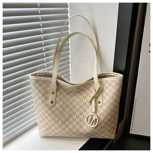 Detail of beige tote bag featuring monogram M pattern and metallic circular charm logo
