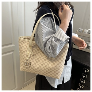 Detail of beige tote bag with M-letter monogram print and metallic logo pendant