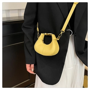 Détail du petit sac demi-lune jaune avec boucle dorée sur un mannequin en tailleur noir