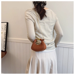 Sac à main plissé caramel avec chaîne dorée et poignée en métal porté par un modèle
