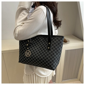 Close-up of large gray tote bag with M-pattern and golden metal logo pendant detail