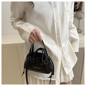 Detail of black pebbled leather bucket bag with gold lettering held by a model