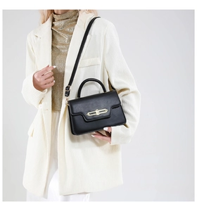 Close-up of minimalist black crossbody bag with sleek gold bar metal lock on white blazer