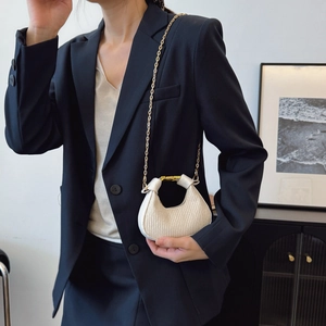 Sac à main croissant plissé beige chic avec chaîne dorée porté par un mannequin en costume