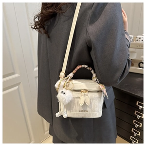 Close-up of white leather handbag with silk scarf detail and plush charm decoration