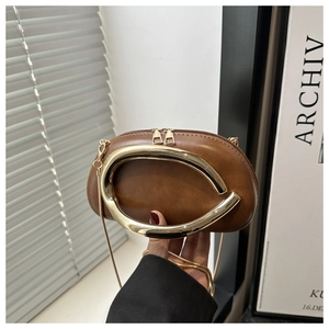 Close-up of brown leather bag featuring large gold metal arc handle and double zipper