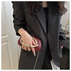 Dettaglio borsa ovale bordeaux con manico in metallo dorato e catena su blazer nero